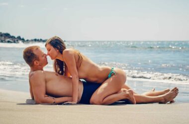 man lying on sand while woman kissing him
